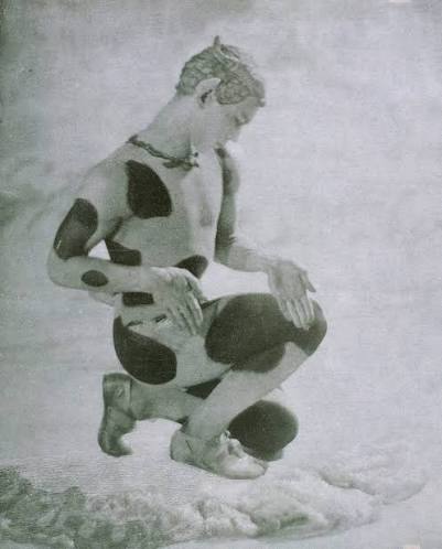 Nijinsky en faune, accroupi, le corps de profil et le buste presque de face : un genou plié très bas vers le sol, le pied de derrière posé sur les orteils, les deux mains refermées sur le genou, la tête penchée de côté vers ses mains.